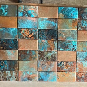 Puede incluir: Una pared enlosada con pequeñas baldosas rectangulares en tonos marrones, azules y verdes, que recuerdan a una pátina de cobre.