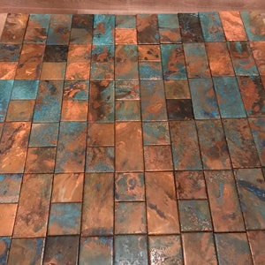 May include: A close-up of a copper tile mosaic with a mix of blue and brown tones. The tiles are arranged in a staggered pattern, creating a unique and textured surface.