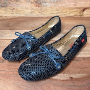 Könnte beinhalten: Ein Paar dunkelblaue Slipper mit strukturiertem Schlangenledermuster, abgerundeter Schuhspitze und einer dekorativen Schleife auf der Vorderseite. Die Schuhe haben goldfarbene Metallösen und ein goldenes Innenfutter mit einer kleinen roten Lasche.