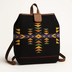 May include: Black backpack with a geometric pattern in yellow, orange, green, and purple. The backpack has brown leather straps, a top handle, and a flap closure. The bag is approximately 12 inches wide and 14 inches tall.