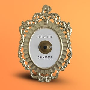 Puede incluir: Timbre de pared dorado y ornamentado con el texto "PRESS FOR CHAMPAGNE" sobre un fondo ovalado blanco. El timbre tiene un marco decorativo y un botón central.