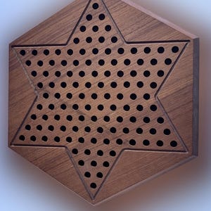 Op de afbeelding: Een zeshoekig houten bordspel met een stervormig ontwerp. De ster is gevuld met kleine gaatjes. Het bord is gemaakt van donkerbruin hout, met een groef die de ster omlijnt.