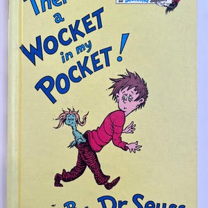 Könnte beinhalten: Ein Kinderbuchcover mit dem Titel "There's a Wocket in my Pocket!" in blauer Schrift. Das Cover zeigt eine Illustration eines Jungen mit einem Wesen, das aus seiner Hose kommt. Der Name des Autors, Dr. Seuss, steht unten.