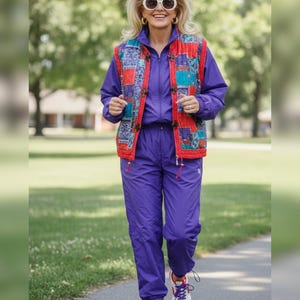 Puede incluir: Un chándal morado vibrante con un chaleco a juego con un diseño de retazos en rojo, azul y morado. El conjunto se combina con zapatillas blancas con detalles morados y gafas de sol redondas.