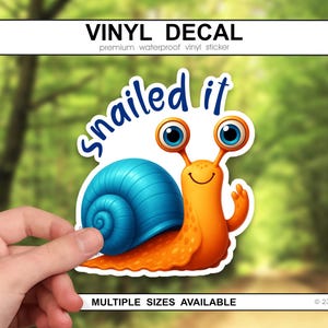 May include: A vinyl decal featuring a cartoon snail with a blue shell and orange body. The snail has large blue eyes and is giving a thumbs up. The text "snailed it" is above the snail. The decal is a waterproof vinyl sticker.