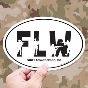 May include: White oval sticker with black text that reads "FLW" with a silhouette of a soldier holding a rifle in each letter. Below the letters is the text "FORT LEONARD WOOD, MO".