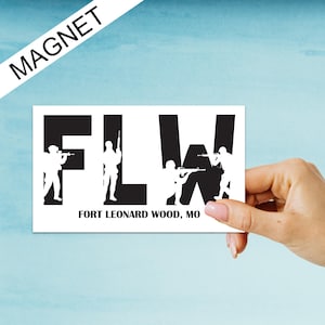 May include: Black and white magnet with the letters "FLW" in large, bold font. The letters are outlined in white and filled in black. The text "FORT LEONARD WOOD, MO" is printed in white below the letters. Silhouettes of soldiers holding rifles are positioned within the letters.