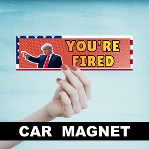 May include: A red, white, and blue car magnet with the text "YOU'RE FIRED" in yellow and orange letters. A photo of Donald Trump is in the background. The magnet says "CAR MAGNET" at the bottom.