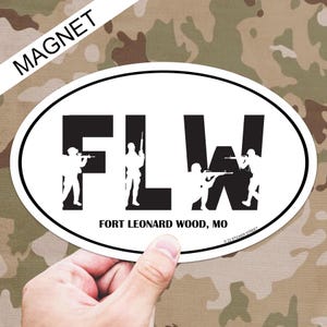 May include: White oval magnet with black text that reads "FLW" with a silhouette of a soldier holding a rifle in each letter. Below the letters is the text "FORT LEONARD WOOD, MO".