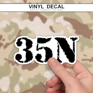 May include: A vinyl decal sticker featuring the black text 35N in a distressed, weathered font style. The sticker has a white border and is shaped to follow the contour of the alphanumeric characters, creating a bold and high-contrast graphic design.
