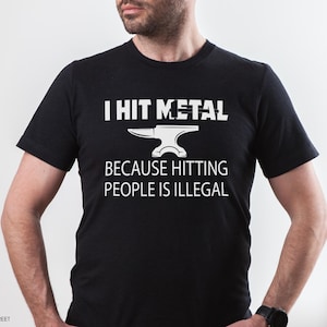 May include: A black short-sleeved t-shirt featuring white text that reads I HIT METAL BECAUSE HITTING PEOPLE IS ILLEGAL, accompanied by a graphic of an anvil centered between the lines of text on the front of the garment.