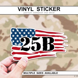 May include: Vinyl sticker with a distressed American flag design and the number "25B" in black. The sticker has a white border and is labelled "VINYL STICKER" at the top. The background is a camouflage pattern.