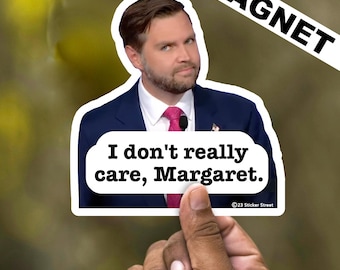 May include: A white magnet with a photo of a man in a suit and tie. The text on the magnet reads "I don't really care, Margaret."  The magnet is held by a hand.
