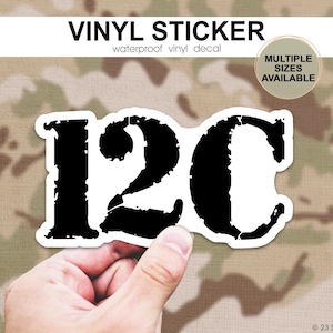 May include: A black and white vinyl sticker featuring the letters "12C" in a bold, distressed font. The sticker is waterproof and available in multiple sizes. The background has a camouflage pattern.