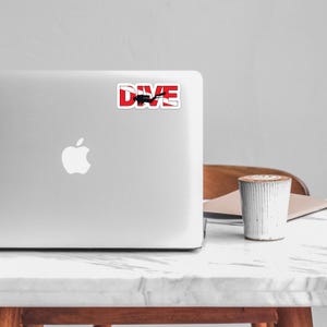 May include: A rectangular sticker featuring the word DIVE in bold white capital letters against a red background. A black silhouette of a scuba diver is positioned in the center of the letter I, with the diver extending horizontally across the design.