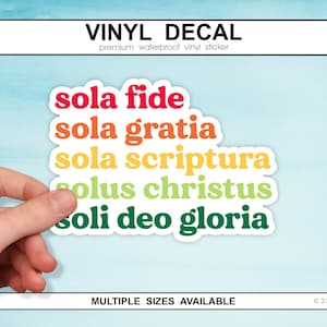 Puede incluir: Una calcomanía de vinilo con las palabras "sola fide, sola gratia, sola scriptura, solus christus, soli deo gloria" en un arcoíris de colores. La calcomanía es sostenida por una mano sobre un fondo azul claro. El texto "VINYL DECAL" está en la parte superior.