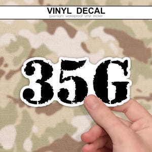 May include: A vinyl decal sticker featuring the black text 35G in a distressed, bold font style. The sticker has a white border and is presented against a camouflage pattern background with the text VINYL DECAL at the top of the image.