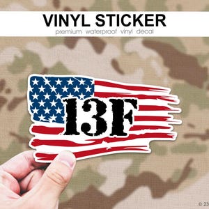 May include: A vinyl sticker featuring a distressed American flag design with red, white, and blue colors. The bold black text 13F is centered over the flag graphic. The sticker has a white border and a rectangular shape with frayed edges.