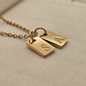 May include: Gold necklace with two small rectangular pendants, one engraved with the letter 'S' and the other with the letter 'A'.