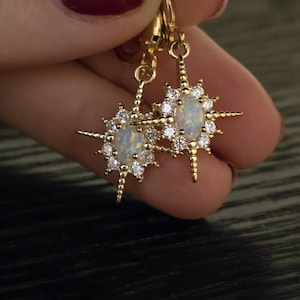 May include: A pair of gold starburst earrings with opal stones and clear cubic zirconia accents.