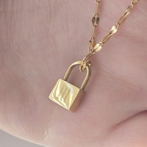 Op de afbeelding: Een gouden ketting met een hangertje in de vorm van een hangslot. Het hangslot heeft de letter "H" gegraveerd.