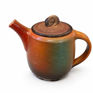 May include: A ceramic teapot with a lid and handle. The teapot has a gradient color scheme, transitioning from orange to green. The lid features a small, rounded knob. The body of the teapot has a textured pattern.