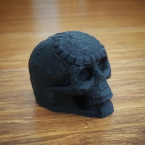 Op de afbeelding: Een zwarte 3D-geprinte schedel met gedetailleerde kenmerken. De schedel is gemaakt van plastic en heeft een gladde, matte afwerking.