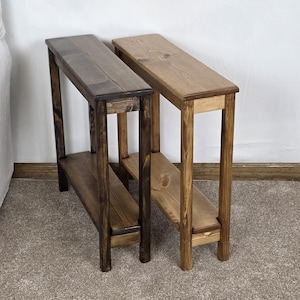 May include: Two wooden side tables, one stained dark brown and the other natural wood. Each table has a long, narrow top and a lower shelf, supported by four legs. The tables are approximately 30 inches long.
