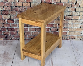 May include: A small, wooden side table with a natural finish. The table has a rectangular top and a lower shelf, supported by four sturdy legs. The table measures approximately 24 inches long, 12 inches wide, and 24 inches high.