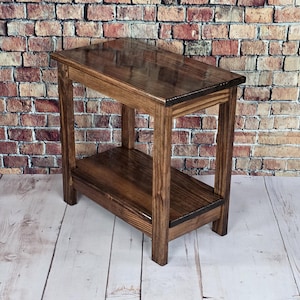May include: A handcrafted wooden side table with a rich, dark stain. The table features a rectangular top and a lower shelf, supported by four sturdy legs. The table measures approximately 30 inches long, 12 inches wide, and 28 inches high.