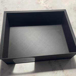 May include: A black plastic storage box with a rectangular opening on the front. The box is empty.