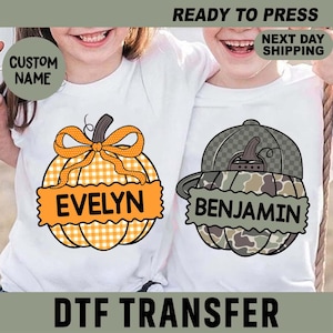 May include: Two white t-shirts featuring pumpkin graphics. The left pumpkin has an orange gingham pattern with a bow and the name EVELYN. The right pumpkin has a camouflage pattern with a baseball cap and the name BENJAMIN. Text includes CUSTOM NAME.