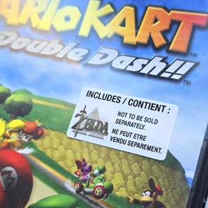May include: A video game case for Mario Kart Double Dash!! with a blue and white background. The case includes a sticker with the text "INCLUDES/CONTIENT : NOT TO BE SOLD SEPARATELY. NE PEUT ETRE VENDU SEPAREMENT."