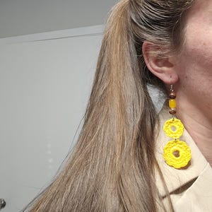 May include: Yellow crocheted earrings with brown wooden beads. The earrings are hanging from a person's ear.