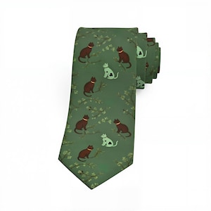 May include: A sage green necktie featuring a repeating pattern of dark brown cats perched on thin branches and light mint green cats with dark clover-shaped markings on their bodies. The design includes small light green leaves scattered throughout.