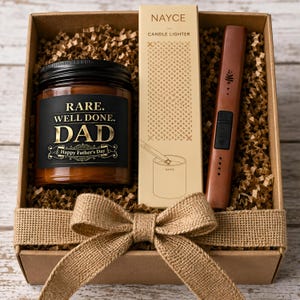 May include: A gift box containing a brown candle in a glass jar with a black label reading RARE. WELL DONE. DAD Happy Father's Day, a tall rectangular box labeled NAYCE CANDLE LIGHTER, and a brown electronic candle lighter with a burlap ribbon.