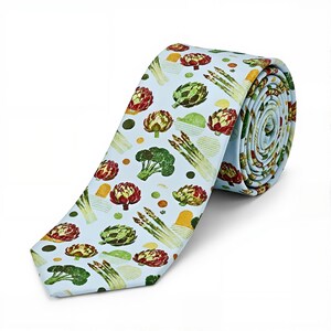 May include: A light blue necktie featuring a repeating pattern of vegetables including red and green artichokes, green asparagus stalks, and broccoli florets, interspersed with small yellow and green circular and rectangular shapes.