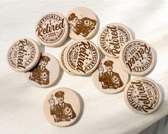 May include: A collection of wooden round ornaments with the text "Officially Retired 2025" and a cartoon image of a person in a police uniform. Some of the ornaments have a middle finger raised.