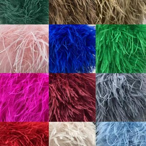 May include: A grid of colorful ostrich feather plumes in shades of green, brown, pink, blue, and red. The feathers have a soft, fluffy texture and are arranged in a square pattern. The colors range from dark to light, creating a visually appealing display.