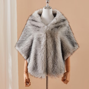 May include: A grey and brown faux fur cape, shown on a mannequin. The cape has a hood and a V-neck. The fur looks soft and fluffy, giving a luxurious appearance. The cape is designed to be worn over the shoulders, offering warmth and style.