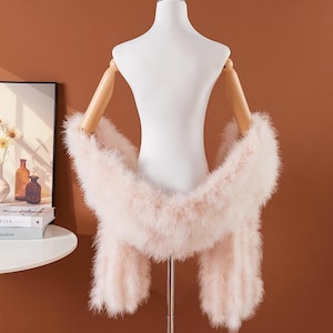 May include: A pale pink feather boa displayed on a white mannequin. The boa has a fluffy, voluminous design, appearing soft to the touch. The background is a warm, solid brown colour.