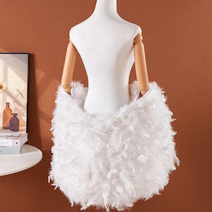 May include: A white, fluffy feather skirt is displayed on a mannequin. The skirt is made of soft, white feathers and is designed to be worn around the waist. The mannequin has wooden arms and is set against a brown background.