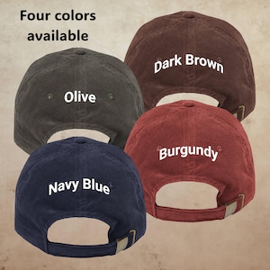 Op de afbeelding: Vier corduroy baseballpetten in olijf, donkerbruin, bordeauxrood en marineblauw. Elke pet heeft een verstelbare band en is gelabeld met zijn kleur. De tekst "Vier kleuren beschikbaar" staat bovenaan.
