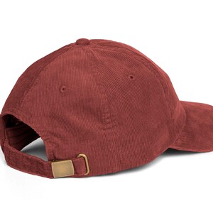 Op de afbeelding: Een bordeauxrode corduroy baseballcap met een gebogen klep. De cap heeft een verstelbare gespsluiting in messingkleur aan de achterkant. De cap is gemaakt van een zachte, getextureerde stof.