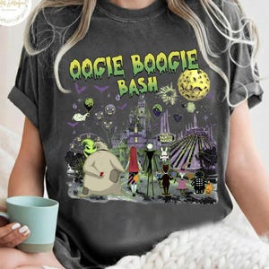 May include: Dark gray t-shirt with the text "Oogie Boogie Bash" in yellow and green. The shirt features a colorful graphic of characters and scenes from a Halloween-themed movie, including a full moon and a haunted house.