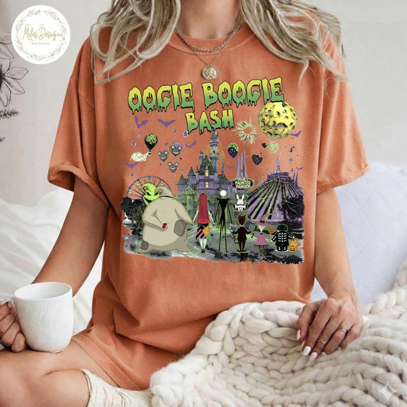 May include: Orange short-sleeved t-shirt with a graphic featuring characters and elements from "The Nightmare Before Christmas." The text "Oogie Boogie Bash" is displayed above the graphic. The shirt is worn by a person.