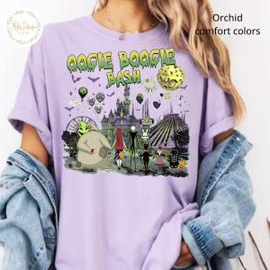 May include: A light purple t-shirt with a graphic featuring characters and elements from "The Nightmare Before Christmas." The design includes the text "Oogie Boogie Bash" in green and yellow, along with a haunted house and other spooky imagery.