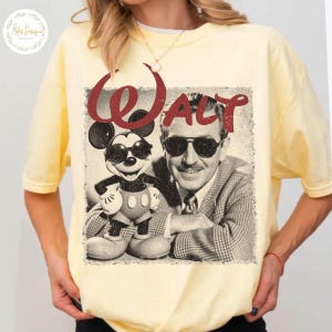 May include: A pale yellow t-shirt with a retro graphic of Mickey Mouse and Walt Disney wearing sunglasses. The word "WALT" is printed in red above the image. The shirt has short sleeves and a crew neck.