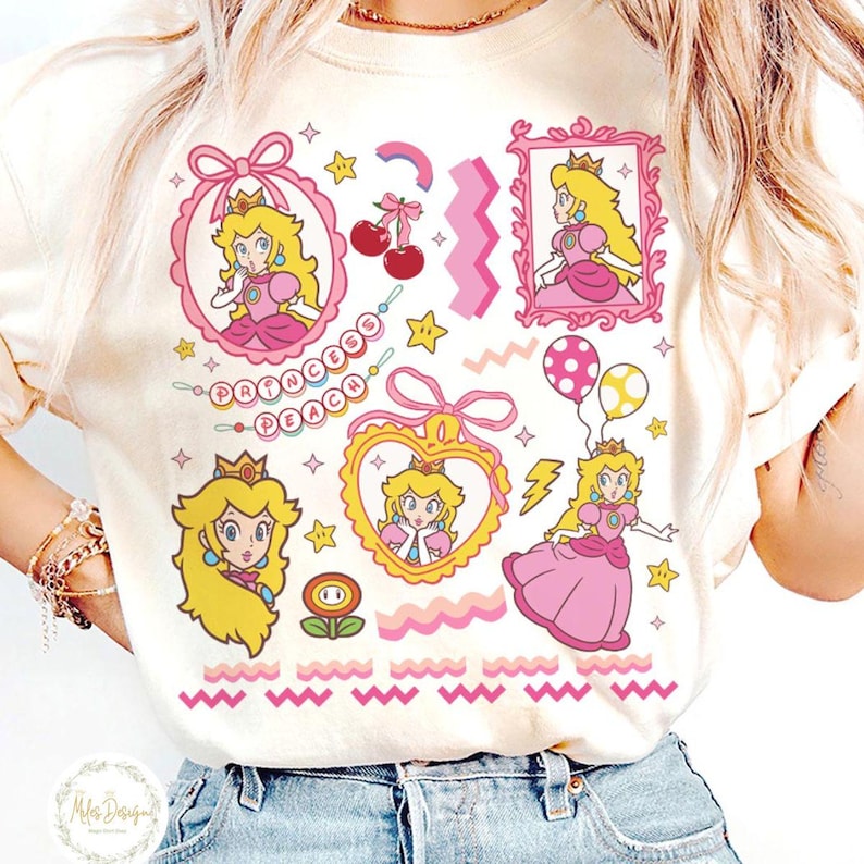 May include: Cream-colored t-shirt featuring a Princess Peach graphic. The design includes multiple images of Princess Peach in pink dresses, crowns, and various decorative elements like stars, cherries, and the text "PRINCESS PEACH".