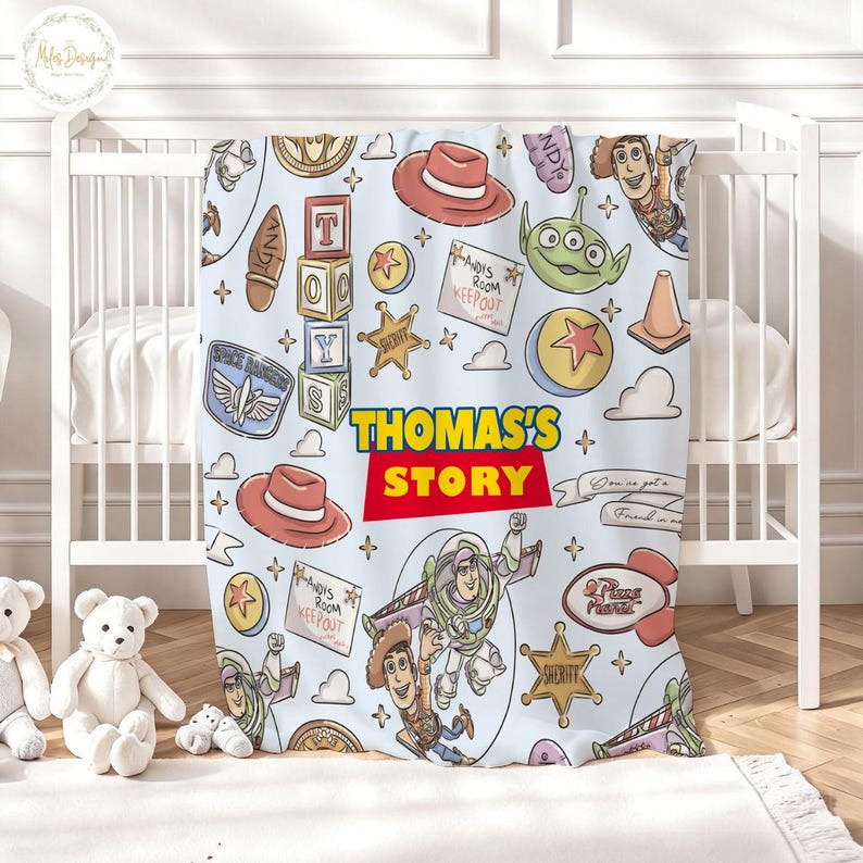 May include: A light blue baby blanket featuring characters and elements from the movie "Toy Story." The blanket includes images of Woody, Buzz Lightyear, and other characters, along with the text "THOMAS'S STORY."